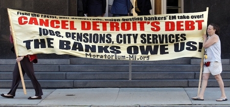 Auch in Detroit wehren sich die Menschen gegen den Ausverkauf.  Text auf dem Transparent: "Schluss mit Detroits Schulden! Arbeit, Rente, kommunale Dienstleistungen - Das schulden uns die Banken!"
